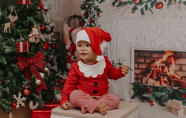 Bebê com roupa de Papai Noel em cenário natalino